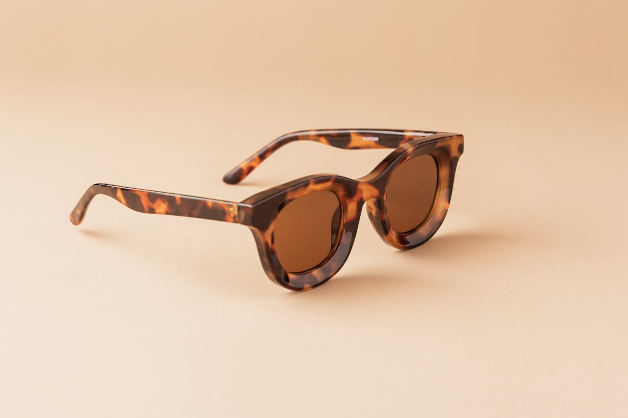 services-02 Elegant tortoiseshell sunglasses with brown lenses creatively displayed on a simple beige backdrop.